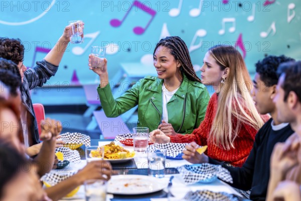 Multiethnic friends enjoying a meal and drinks at a bowling alley restaurant, celebrating their