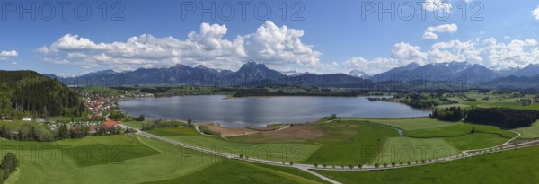 Expansive landscape with a view of Lake Hopfensee and mountains, surrounded by green meadows and a