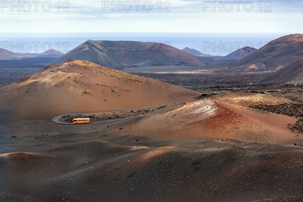 Orange-coloured coach with tourists drives through the fire mountains of Timanfaya National Park,