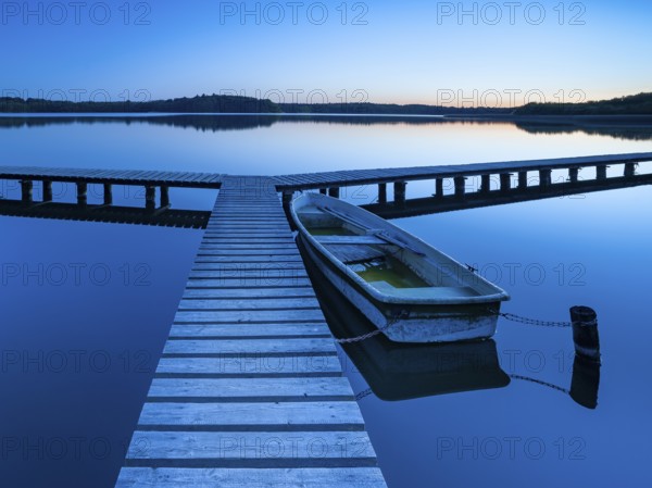 Wooden jetty with rowing boat at dusk, after sunset on Lake Schaalsee, Mecklenburg-Western