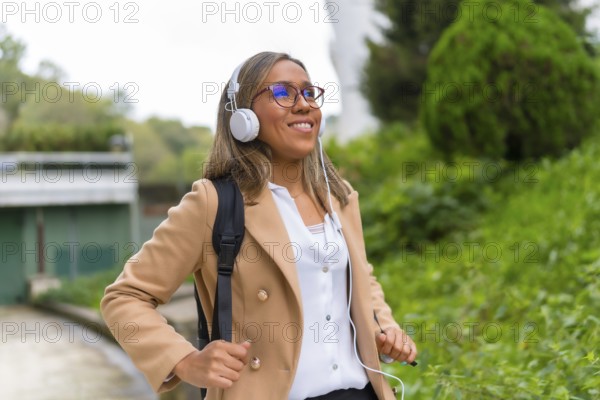 Portrait of a happy latin businesswoman listening to music commuting in the city walking down a