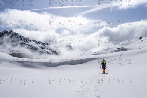 Atmospheric clouds in a wintry mountain landscape, ski tourer on the ascent to Porta d'Es-cha,