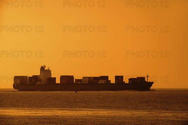 Container ship, containership Amalthea, loaded with containers silhouetted against orange sunset
