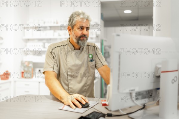 Mature male pharmacist in uniform using computer in the store
