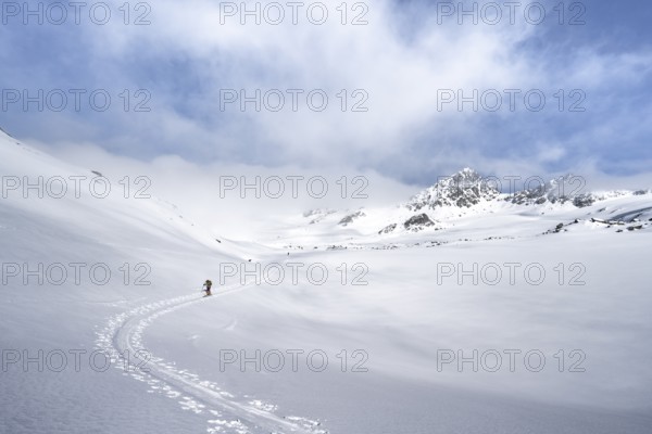 Ski tourers ascending through a picturesque snow-covered mountain landscape with peaks, ascent to