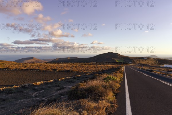 Road leads through hilly volcanic landscape, Famara Mountains, evening sky, Cumulus, Los Valles,