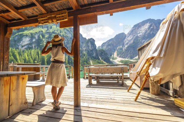 Woman wearing straw hat standing on wooden pier, admiring stunning landscape of lake braies and