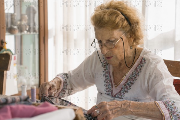 Senior seamstress stitching fabric with concentration in her home workshop, surrounded by colorful