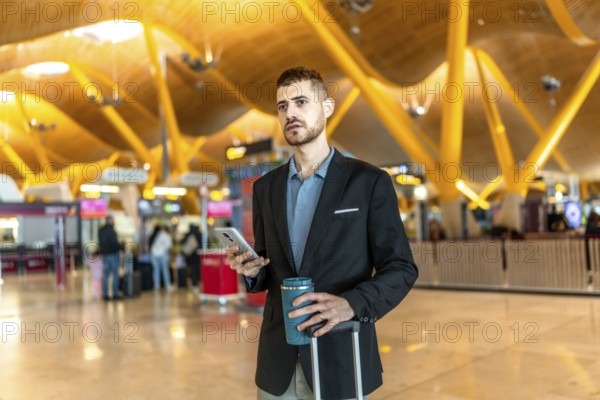 Businessman holding a reusable coffee cup and smartphone while waiting for his flight at the