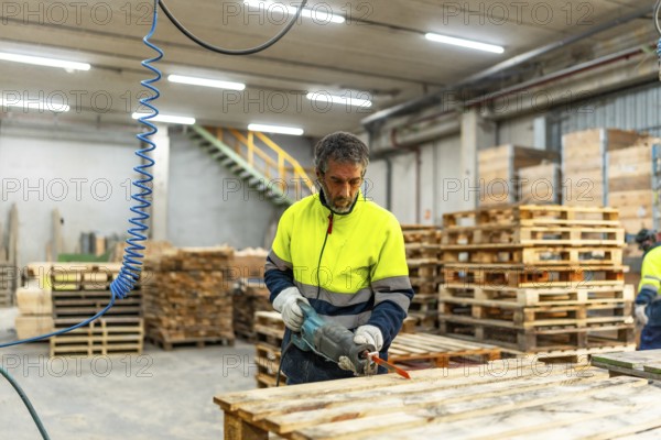 Adult caucasian man worker repairing broken pallets in a recycling plant workshop using compressed