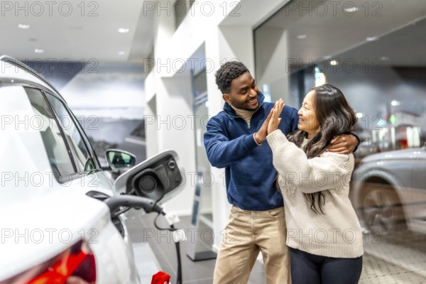 Happy multiethnic couple celebrating their new electric car purchase with a high five at the