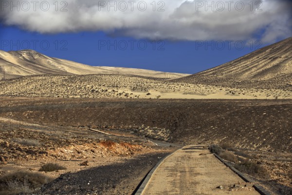 Lonely road in front of a dune landscape under a cloudy sky, Pajara, Fuerteventura, Canary Islands,