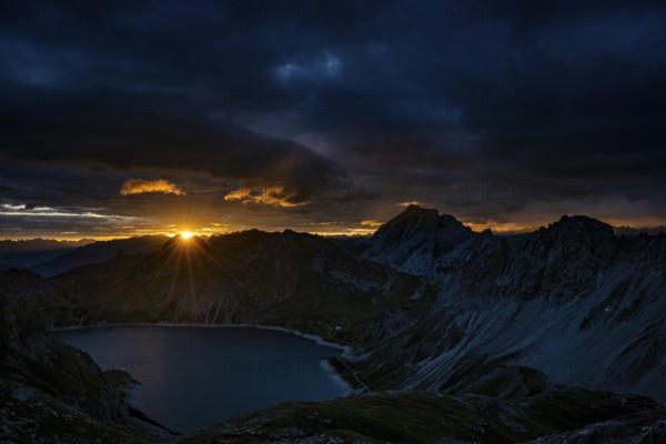 Lake Lüner See with Montafon mountains and dramatic cloudy sky at sunrise, Tschagguns, Rätikon,