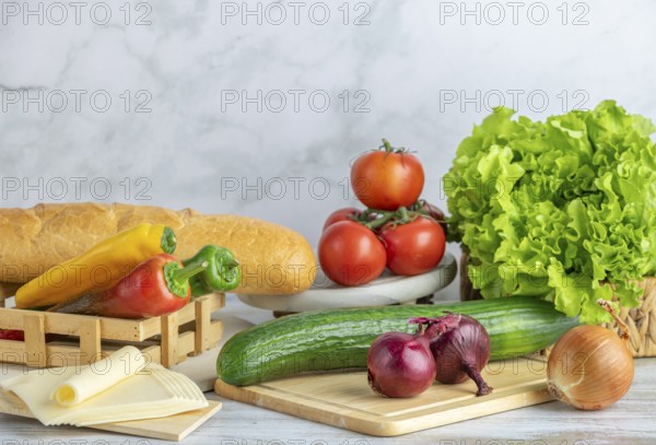 Colourful peppers, tomatoes, cucumber, lettuce and slices of cheese next to a baguette on a table,