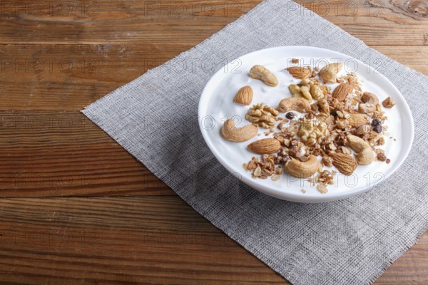 White plate with greek yogurt, granola, almond, cashew, walnuts on brown wooden background. close