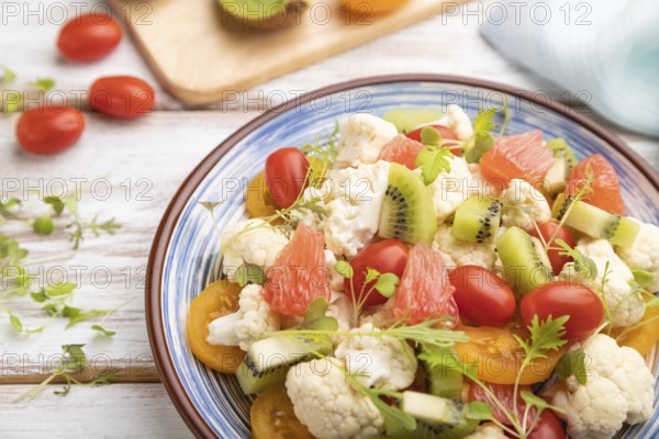 Vegetarian salad of cauliflower cabbage, kiwi, tomatoes, microgreen sprouts on white wooden