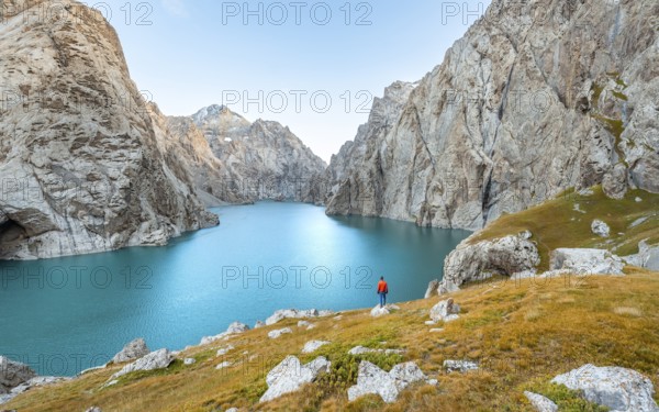 Young man at the turquoise mountain lake Kol Suu with rocky steep mountains, Kol Suu Lake, Sary