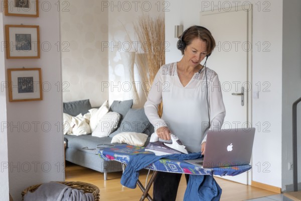 Woman, mid-50s, works from home, with laptop and communicates with colleagues via headset, home