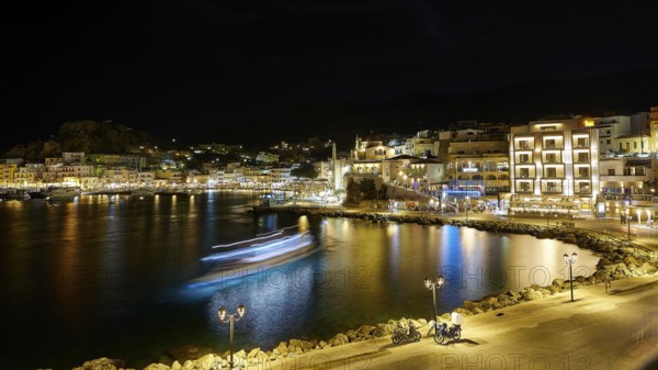 Harbour at night with illuminated buildings, lights reflected in the calm water, Pigadia, town and