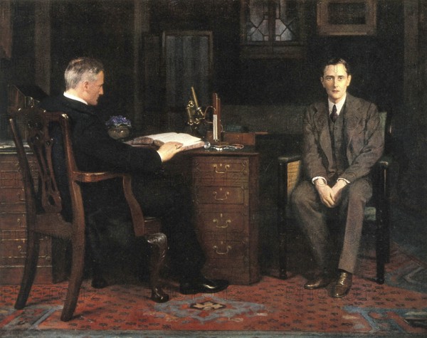 Two men are in an office, one sitting at a desk and the other on a chair, engrossed in a