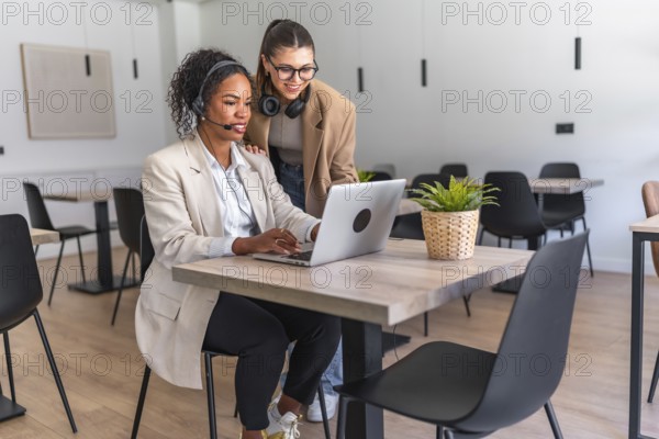 Two businesswomen collaborating on a laptop in a modern office, demonstrating teamwork and