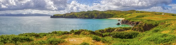 Panoramic view of a picturesque coastal landscape with cliffs, green grass and calm sea under a