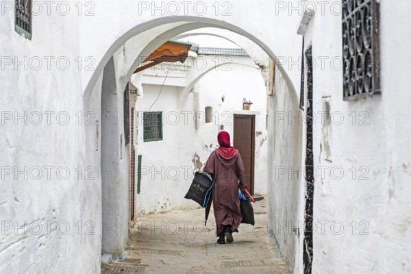Moroccan Muslim woman in traditional Islamic dress wearing hijab walking with shopping bags in