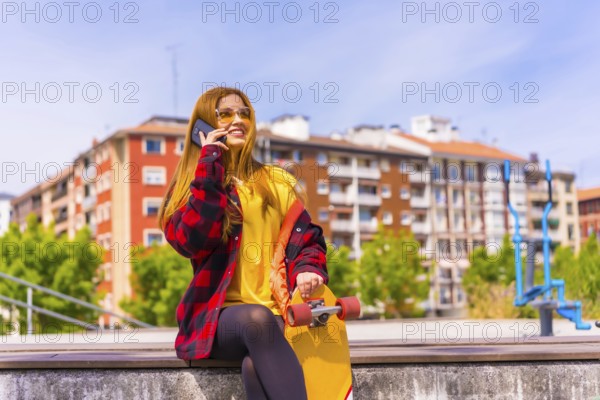 Skater woman in a yellow t-shirt, red plaid shirt and sunglasses, sitting with skateboard in the