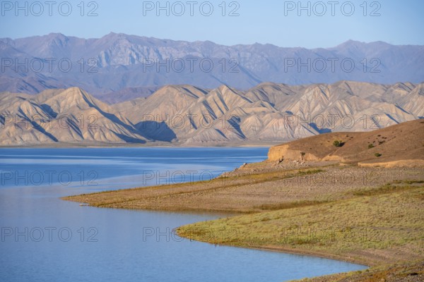 Blue Toktogul reservoir between dry mountain landscape, hilly mountains in the evening light,