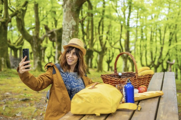 A young Caucasian woman waving on the phone sitting at a picnic table in the woods. Summer
