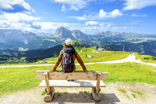 Hiker relaxing on a bench and admiring the odle mountains in val di funes, south tyrol, italy