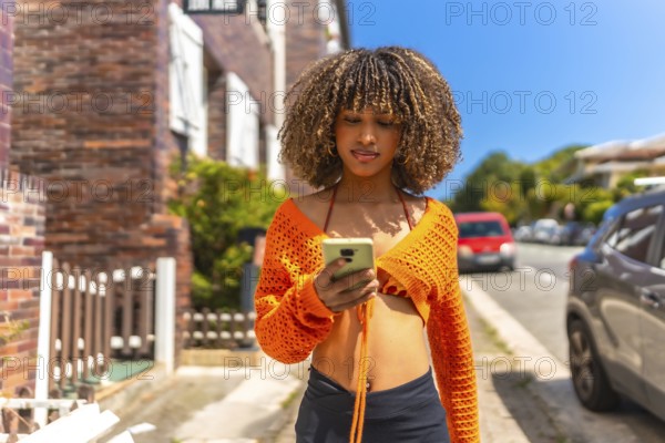 Frontal view of a beauty latin woman with wavy hair and colorful casual clothes using phone walking