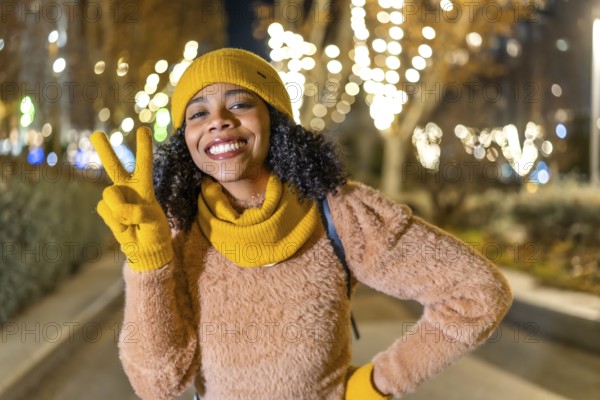 Portrait of a smiling young woman wearing yellow winter clothes showing victory sign with fingers