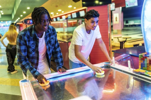Two young men concentrating on playing air hockey in a vibrant entertainment center, enjoying a