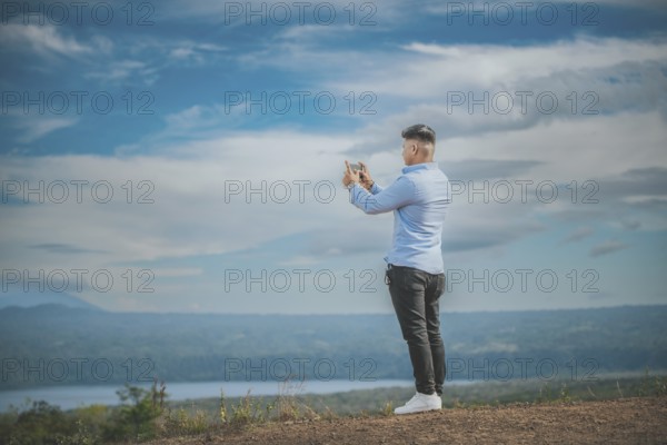 Young man taking photos with cell phone at a natural viewpoint. Tourist taking photos with phone at