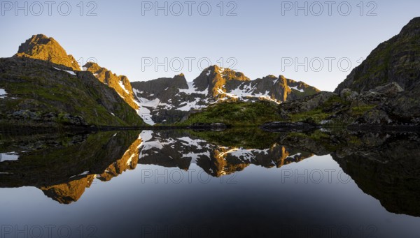 Rocky mountain peaks reflected in a small pond, mountain landscape with alpenglow at sunrise, at