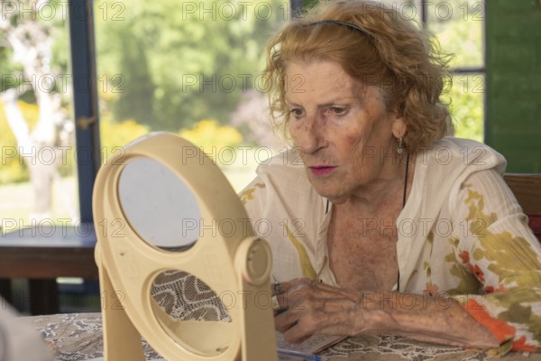 Senior woman applying makeup while gazing at her reflection in a double mirror on a table,