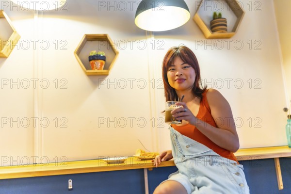 Low angle view portrait of an asian cool young woman smiling at camera sitting drinking coffee in a