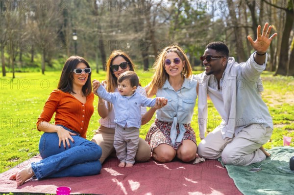 Group of cheerful multi ethnic friends with sunglasses enjoying picnic in a park with a baby boy