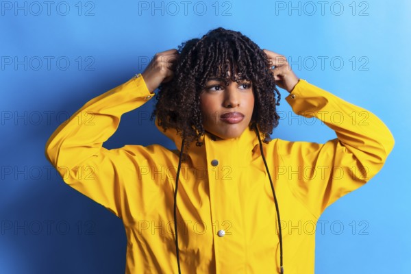 Young woman with curly hair wearing a yellow raincoat adjusting the hood while looking away on a