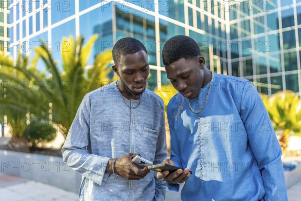 Two senegalese businessmen wearing traditional dashiki attire are using smartphones in front of a