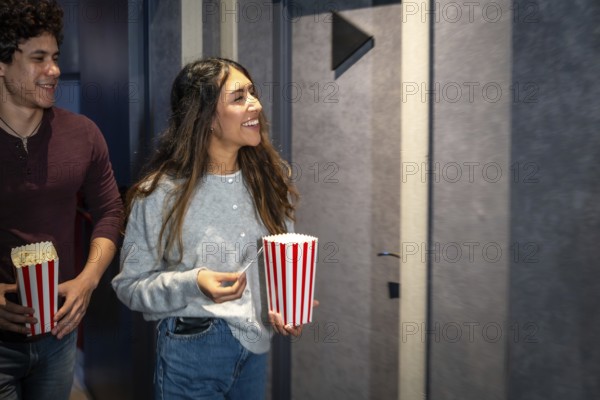 Happy couple walking into a movie theater, holding popcorn buckets and tickets, excited for the