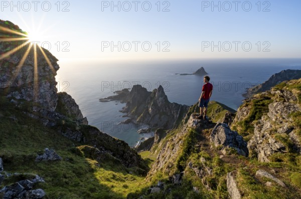 Mountaineer on the summit of Måtind or Måtinden, view of picturesque coastal landscape with sun