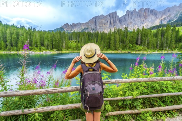 Female hiker with backpack admiring the turquoise waters of lake carezza and the latemar mountain