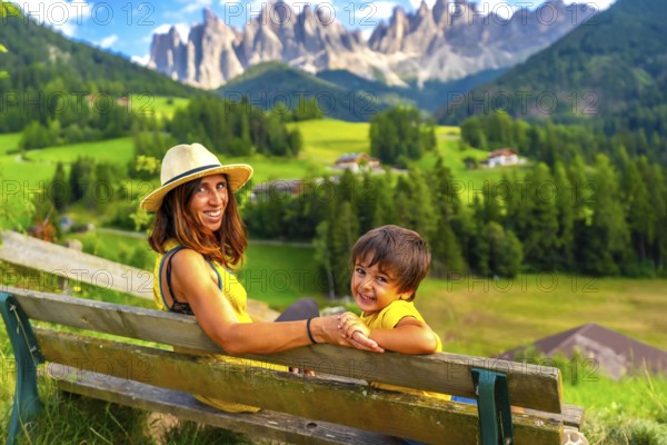 Mother and son sitting on a bench, admiring the breathtaking landscape of the italian dolomites