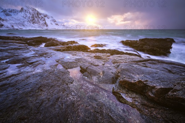 Beach of Norwegian sea on rocky coast in fjord on sunset in winter. Vareid beach, Lofoten islands,