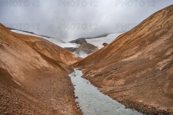 Steaming stream between colourful rhyolite mountains and snowfields, Hveradalir geothermal area,