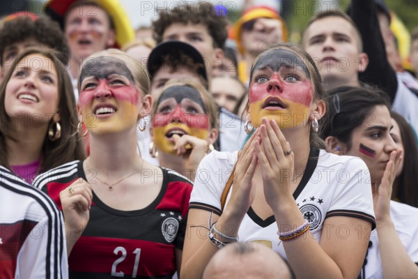 Women wearing make-up in the German national colours watch the football match in the fan zone at