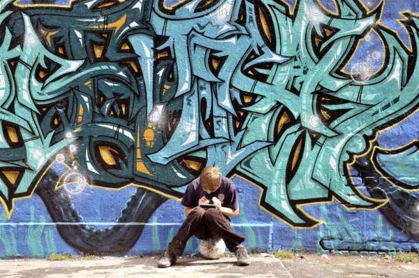 Ten-year-old boy playing with his Nintendo in front of a graffiti wall, football pitch, Germany,
