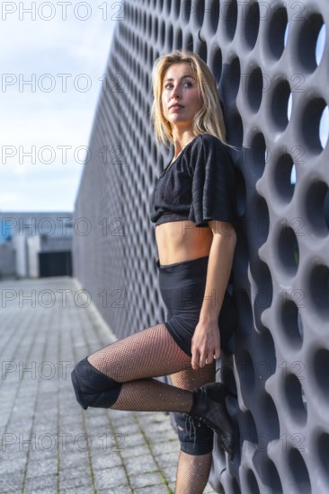 Young urban dancer striking a pose in high heels, knee pads, and fishnet stockings, exuding